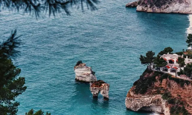 Scogliere mozzafiato e spiagge deserte Italia, con faraglioni che emergono dal mare turchese e una villa panoramica.