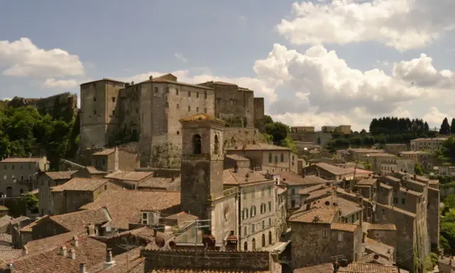 Panoramica di antichi borghi vicino Follonica, con un imponente castello in cima alla collina e un campanile che svetta tra i tetti rossi.