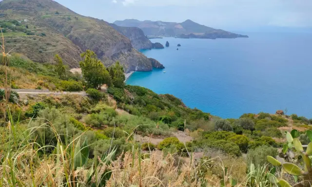Panoramica mozzafiato per capire come visitare le Isole Eolie: costa verdeggiante, mare blu intenso e isole vulcaniche all'orizzonte.