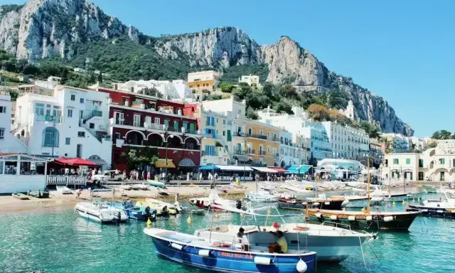 Colorate case affacciate sul mare turchese, con barche ormeggiate e montagne sullo sfondo. Un incantevole scorcio delle isole vicino Napoli.