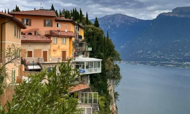 Case colorate aggrappate alla roccia a Tremosine sul Garda, con il lago e le montagne sullo sfondo.