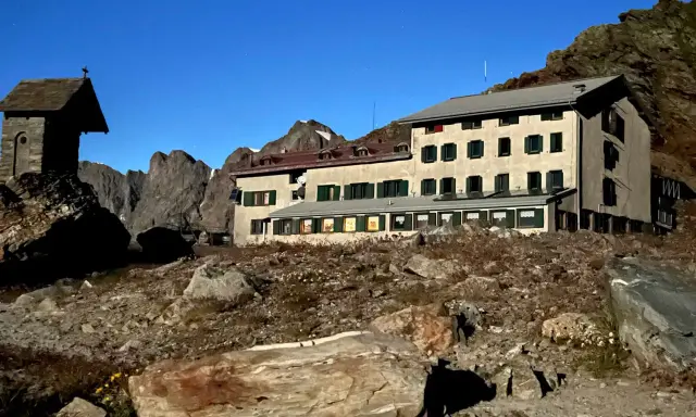 Rifugio alpino con piccola cappella, un esempio di cosa vedere in Lombardia, immerso in un paesaggio roccioso sotto un cielo stellato.