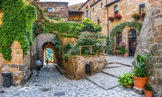 Un vicolo acciottolato tra antichi borghi da visitare nelle Marche, con case in pietra ricoperte di edera e fiori colorati.