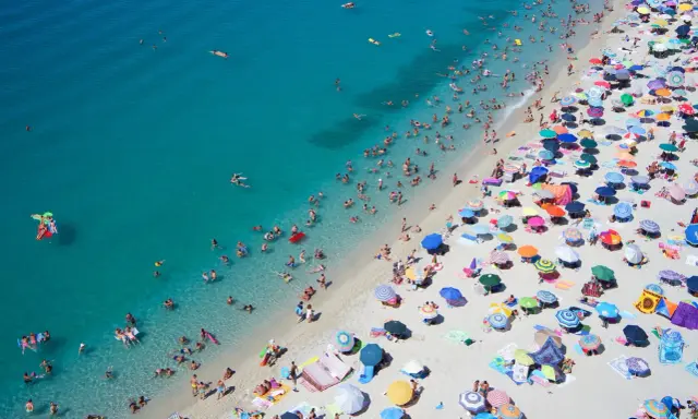 Spiaggia affollata con ombrelloni colorati e bagnanti nell'acqua cristallina, un'immagine perfetta per scoprire le località di mare più economiche in Italia.