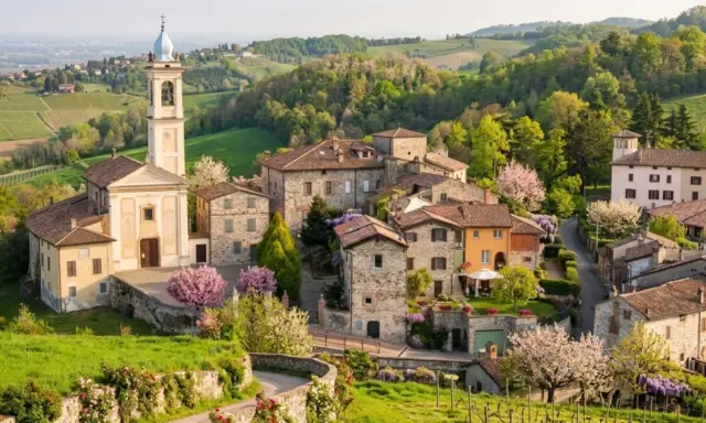 Borgo pittoresco con chiesa e campanile, colline verdi e fiori in primavera. Un luogo incantevole per scoprire cosa vedere a Golferenzo.