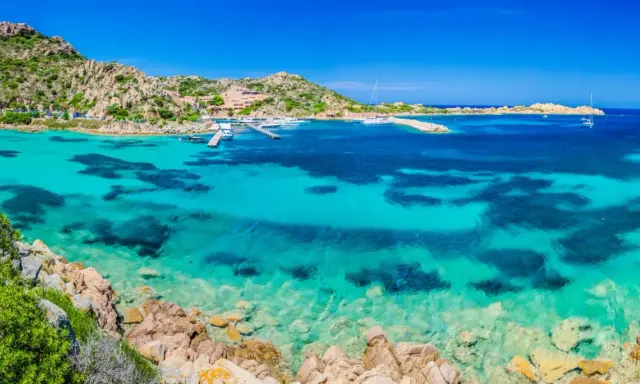 Acque cristalline e rocce granitiche ti aspettano per una visita alla Maddalena. Un paradiso azzurro con barche all'ancora.