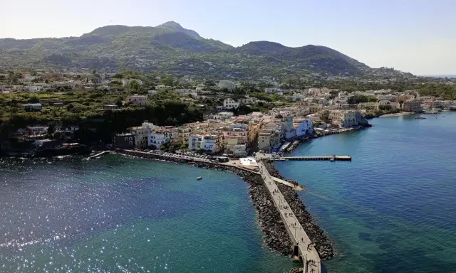 Ischia vista da Napoli: un borgo colorato si affaccia sul mare blu, con montagne verdi sullo sfondo.