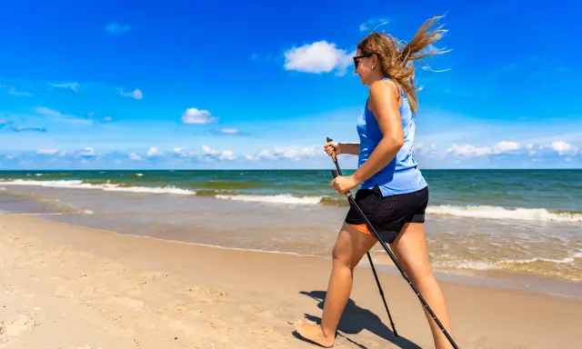 Donna con bastoncini da nordic walking in una splendida passeggiata al mare, con il vento che le scompiglia i capelli.