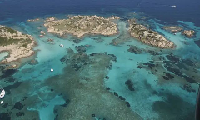Acque cristalline e isolotti rocciosi, un paradiso dove si trova la Maddalena. Barche navigano in questo mare turchese.