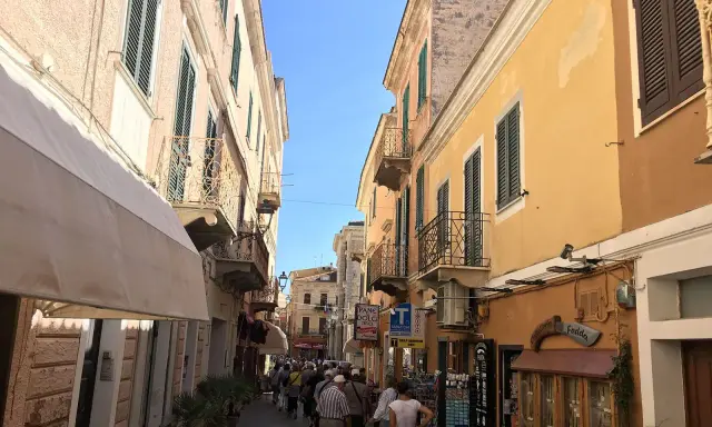 Passeggiata in un vicolo colorato, ideale per visitare La Maddalena in auto, con edifici storici e negozietti.