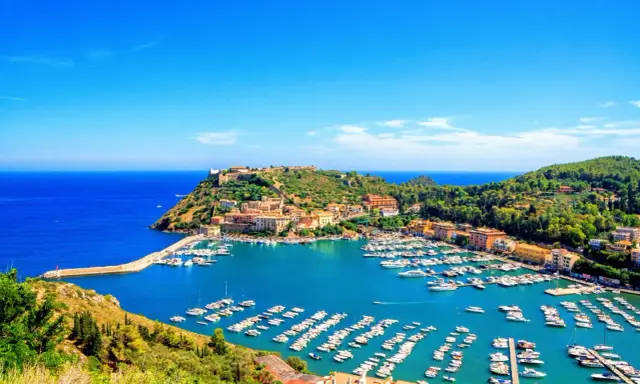 Porto Ercole, con le sue splendide spiagge e il porto pieno di barche, incanta sotto un cielo azzurro.