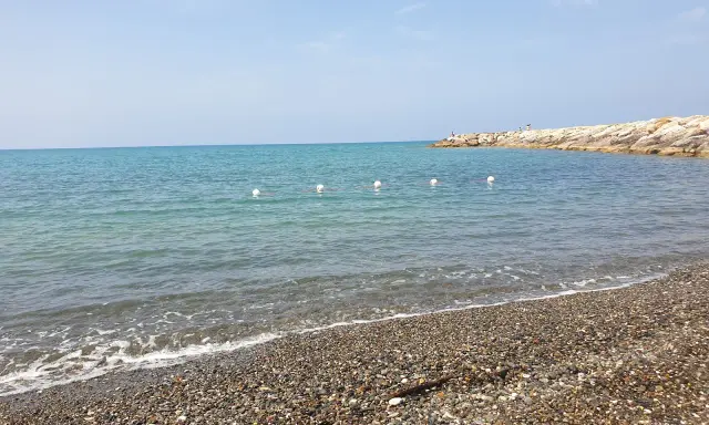 Spiagge più belle della Marina di Cecina: mare azzurro, ciottoli levigati e un molo roccioso con qualche bagnante.