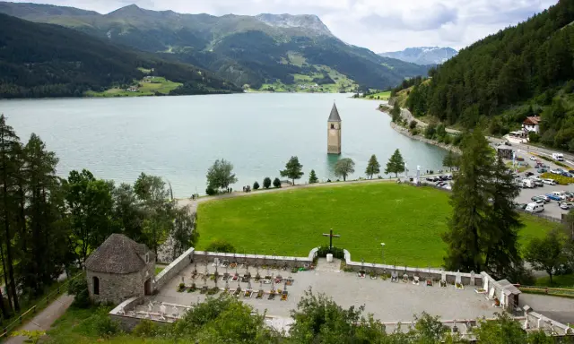Un antico campanile nel lago, circondato da montagne verdi e un cimitero.