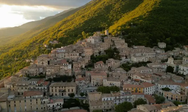 Borgo San Donato, un incantevole paese arroccato su un colle, immerso nel verde di una montagna illuminata dal sole al tramonto.