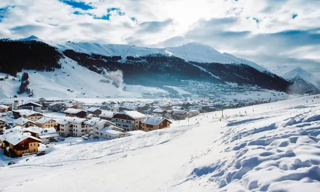 Paesaggio invernale con villaggio innevato e montagne sullo sfondo. Perfetto per sapere dove andare in montagna in Trentino per sciare.