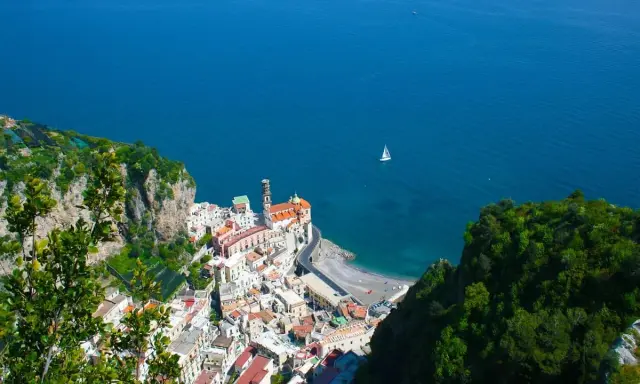 Vista dall'alto di Amalfi, con il mare blu intenso e una barca a vela. Il percorso da Amalfi a Ravello offre panorami mozzafiato.