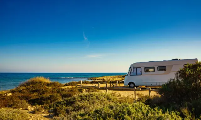 Un camper bianco sosta su un sentiero sabbioso con vista sul mare blu intenso. Un'avventura indimenticabile in camper all'Isola d'Elba.