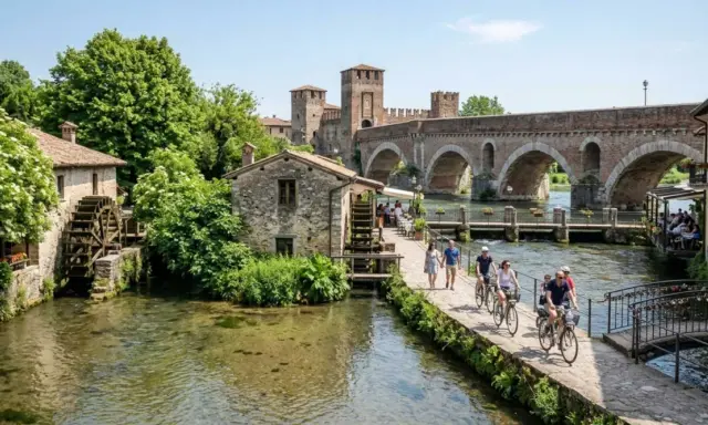 Un pittoresco borghetto sul Mincio con mulini ad acqua, un ponte ad archi e persone che passeggiano e pedalano.