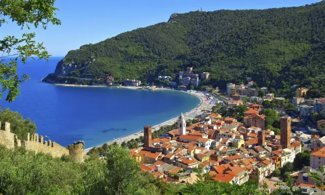 Vista panoramica di pittoreschi liguria paesi sul mare, con case dai tetti rossi che scendono verso una baia azzurra e una spiaggia affollata.