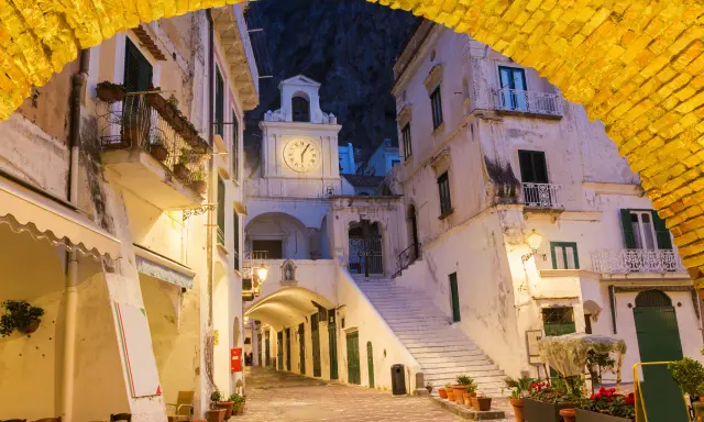 Un vicolo illuminato ad Atrani, con un arco giallo in primo piano e un campanile con orologio sullo sfondo.