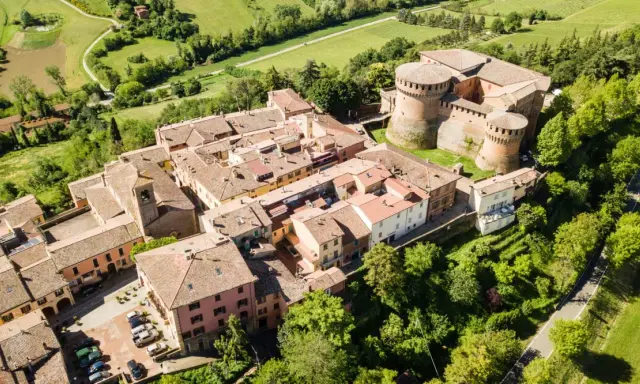 Aerial view of a medieval Italian village with a castle, terracotta roofs, and surrounding green hills.