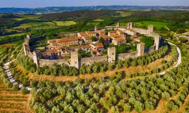 Borghi medievali fortificati vicino Siena, con mura imponenti e torri che dominano un paesaggio collinare verdeggiante.