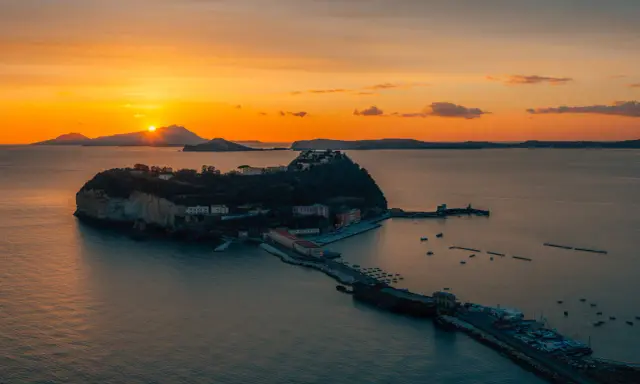 Tramonto infuocato sul golfo di Napoli, con una suggestiva isoletta che emerge dal mare calmo, illuminata dagli ultimi raggi dorati.