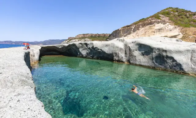 Un uomo nuota in acque cristalline tra scogliere bianche. Un luogo ideale per scoprire le spiagge di Bosa e cosa vedere.