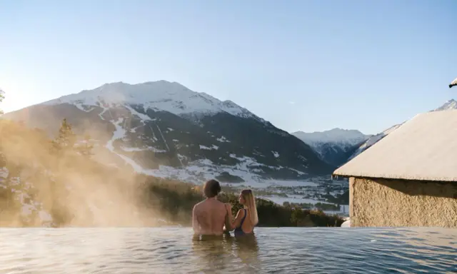 Coppia in una piscina termale con vista sulle montagne innevate. Un'oasi di relax, perfetta per chi cerca terme vicino Milano.