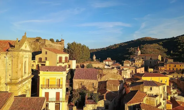 Panoramica di Castiglione di Sicilia al tramonto, con case dai tetti rossi e un castello in rovina su una collina.