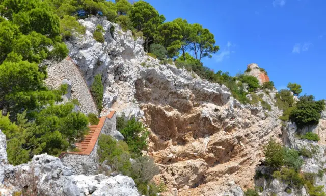 Scogliera rocciosa con una scalinata in mattoni che sale verso la cima, dove si intravede un rudere. Si immagina il **salto di Tiberio** da questo luogo suggestivo.