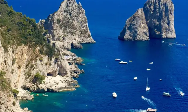 Faraglioni di Capri, tra le più belle isole di Napoli da visitare. Barche navigano nel mare blu intenso.