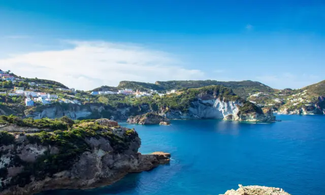 Panoramica della **cala dell'acqua a Ponza**, con case colorate aggrappate alla collina e un mare blu intenso.