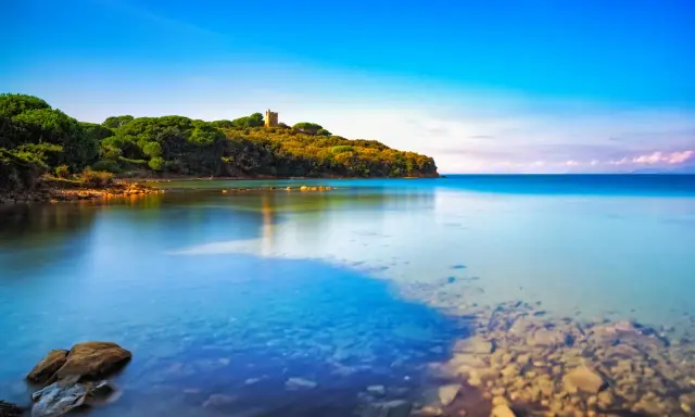 Torre medievale su una collina verdeggiante, con acque cristalline che lambiscono le **punta ala spiagge più belle**.