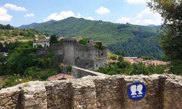 Rovine di un castello a Castiglione di Garfagnana, con un cartello "Kiss... Please" in primo piano.