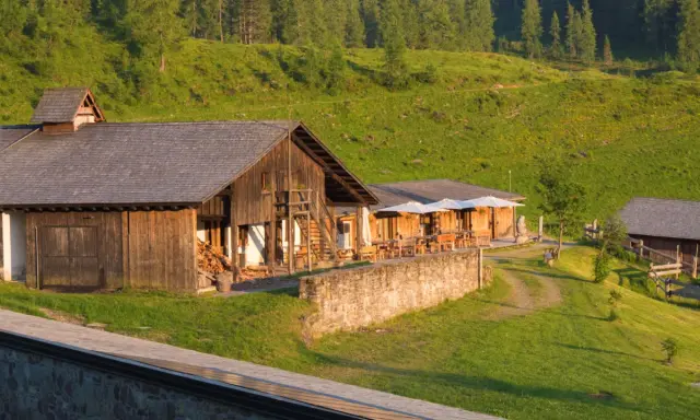 Malghe Alto Adige immerse nel verde, con rustici in legno e tavoli all'aperto sotto ombrelloni bianchi. Un'oasi di pace tra i boschi.