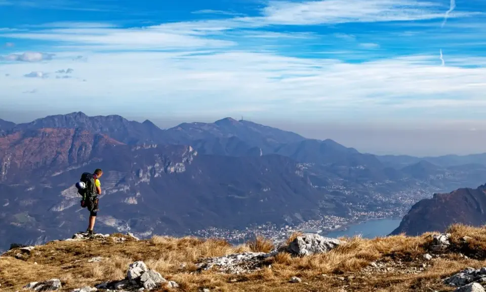 Escursionista ammira la vista panoramica di una montagna vicino Milano, con un lago e un paese in lontananza.