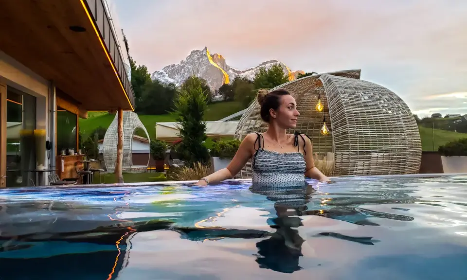 Donna rilassata in una piscina a sfioro con vista sulle montagne illuminate al tramonto, un'esperienza di benessere nelle terme in Trentino Alto Adige.