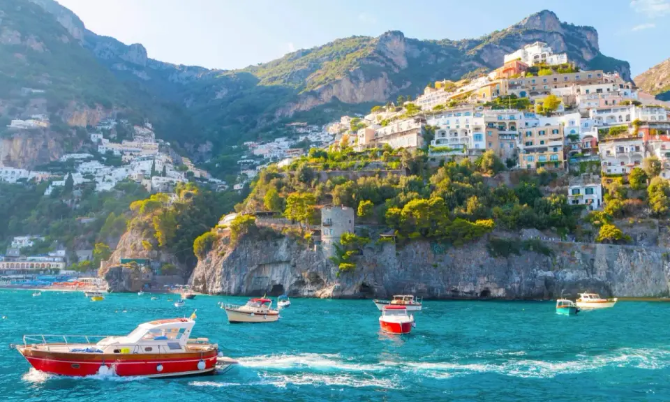 Barche a vela navigano nelle acque turchesi davanti alle case colorate aggrappate alle scogliere delle isole costiera amalfitana.