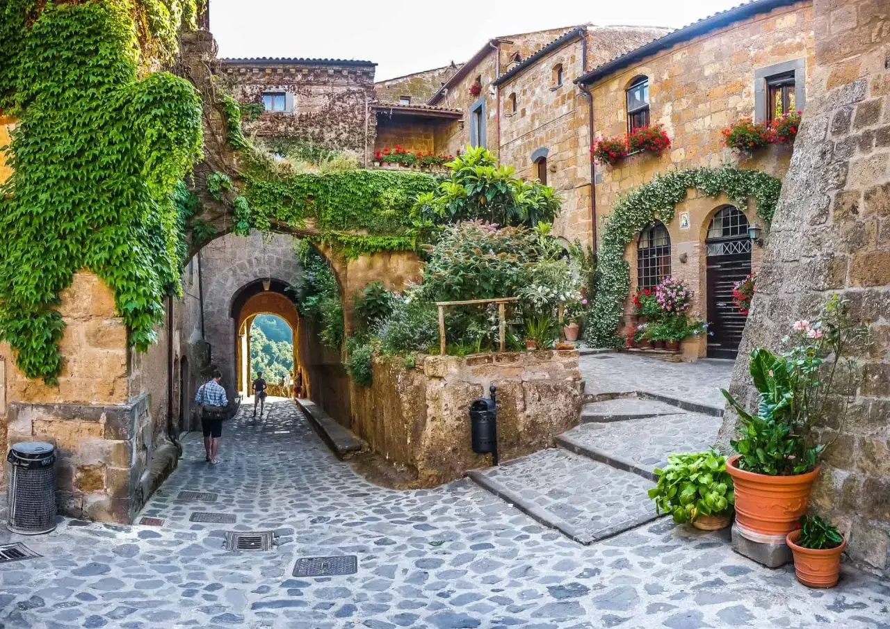 Un vicolo acciottolato tra antichi borghi da visitare nelle Marche, con case in pietra ricoperte di edera e fiori colorati.
