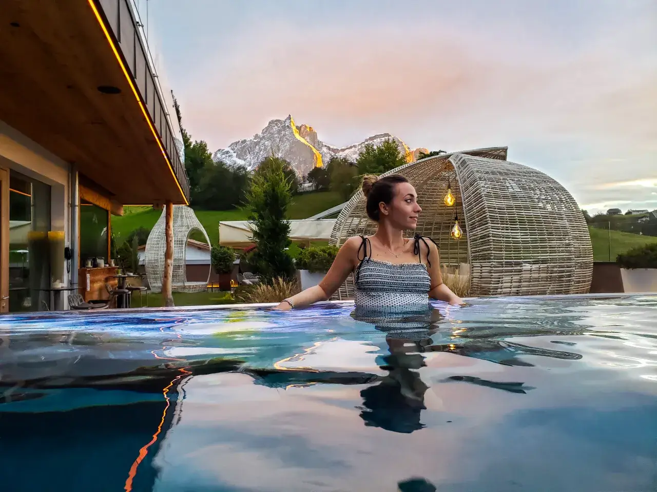 Donna rilassata in una piscina a sfioro con vista sulle montagne illuminate al tramonto, un'esperienza di benessere nelle terme in Trentino Alto Adige.