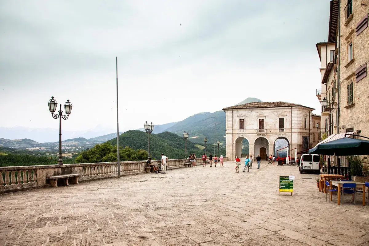 Piazza di Civitella del Tronto con edifici storici, gente che passeggia e vista panoramica sulle colline verdi.