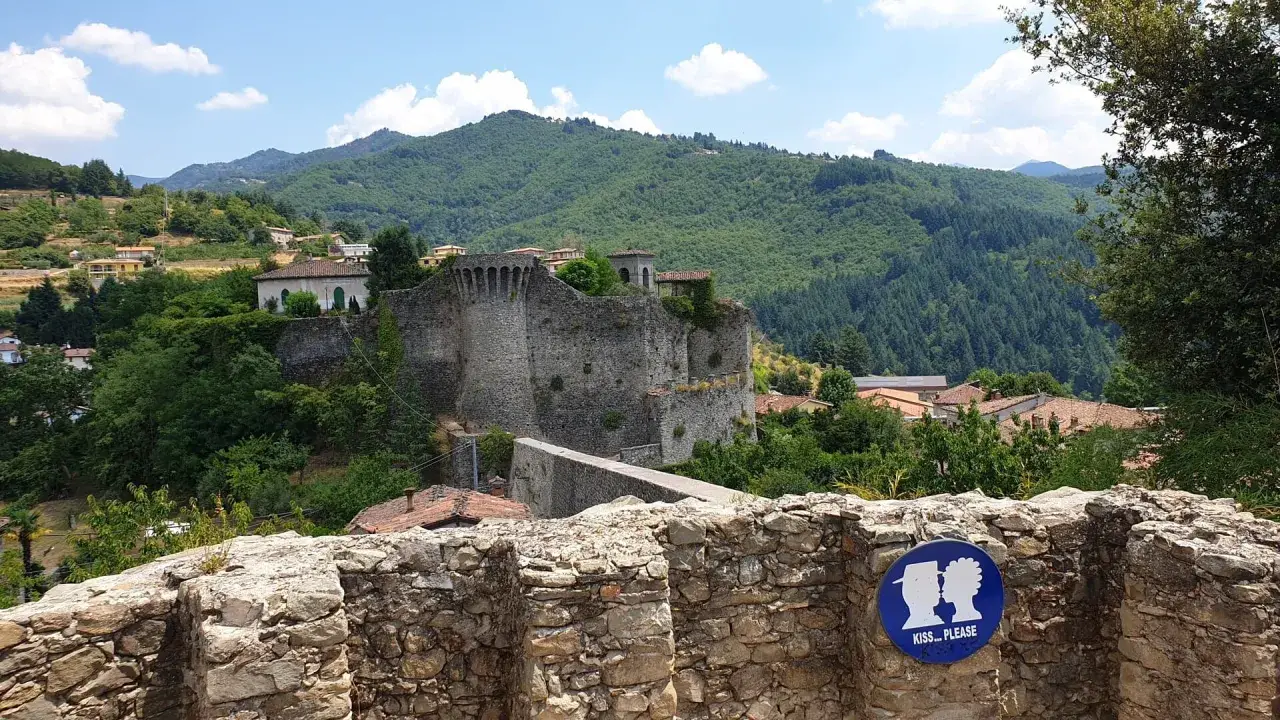 Rovine di un castello a Castiglione di Garfagnana, con un cartello "Kiss... Please" in primo piano.