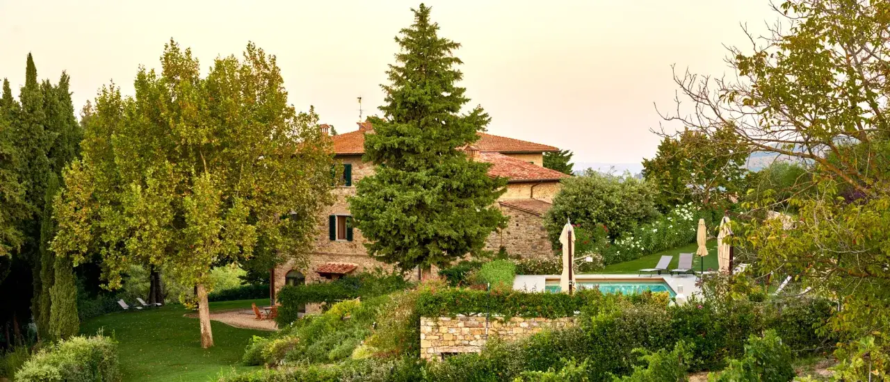 Un casale in pietra con piscina e alberi rigogliosi, un'oasi di pace tra le tenute in Toscana.
