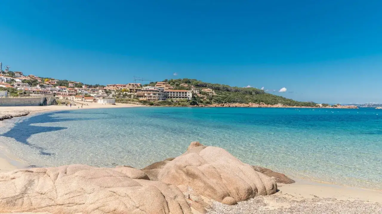 Spiaggia di sabbia chiara e mare cristallino, con case colorate che si affacciano sulla costa. Un angolo di mare bello Italia.