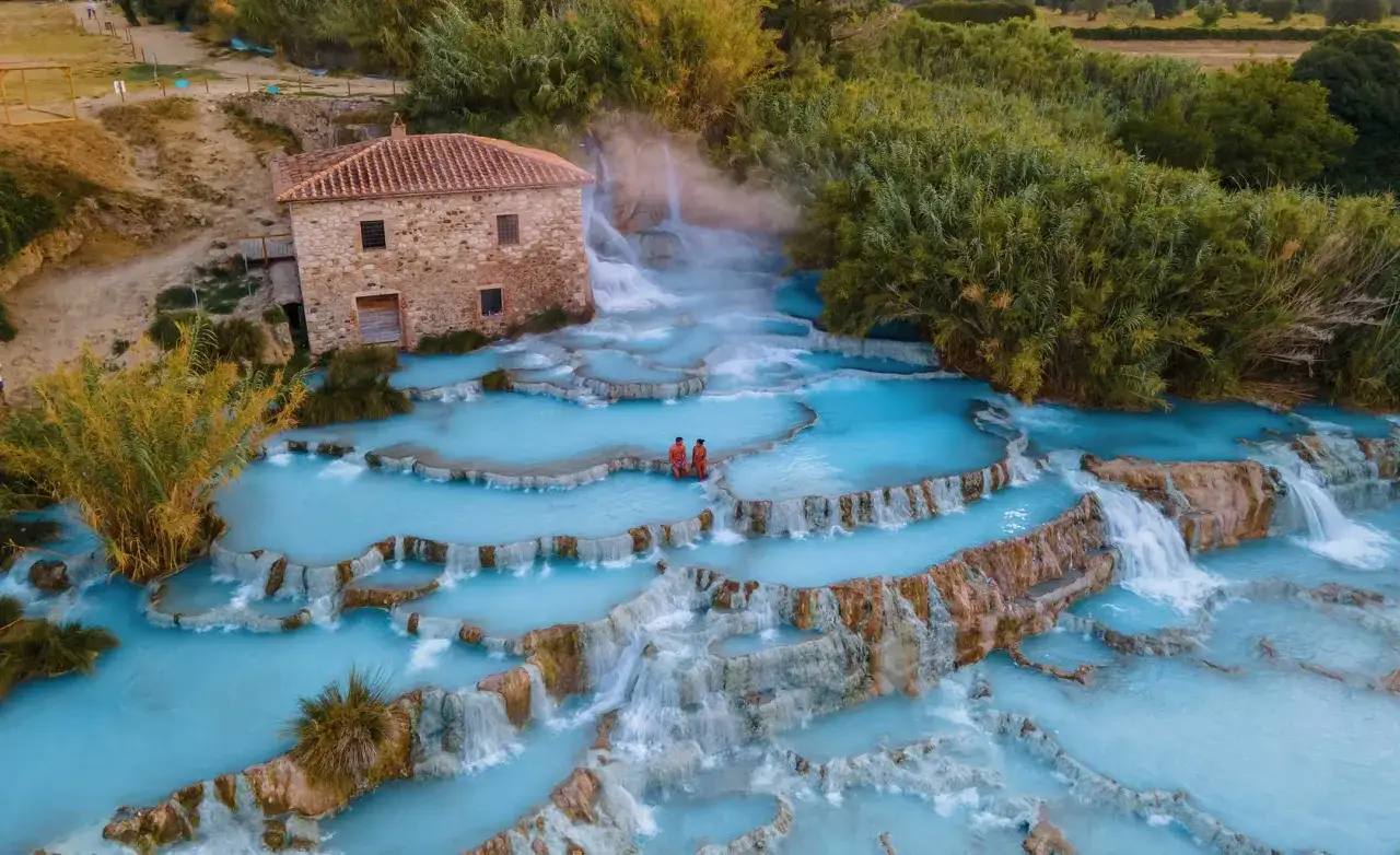 Cascate del Mulino, tra le terme famose in Italia, con un antico casale e coppie che si godono le acque azzurre.