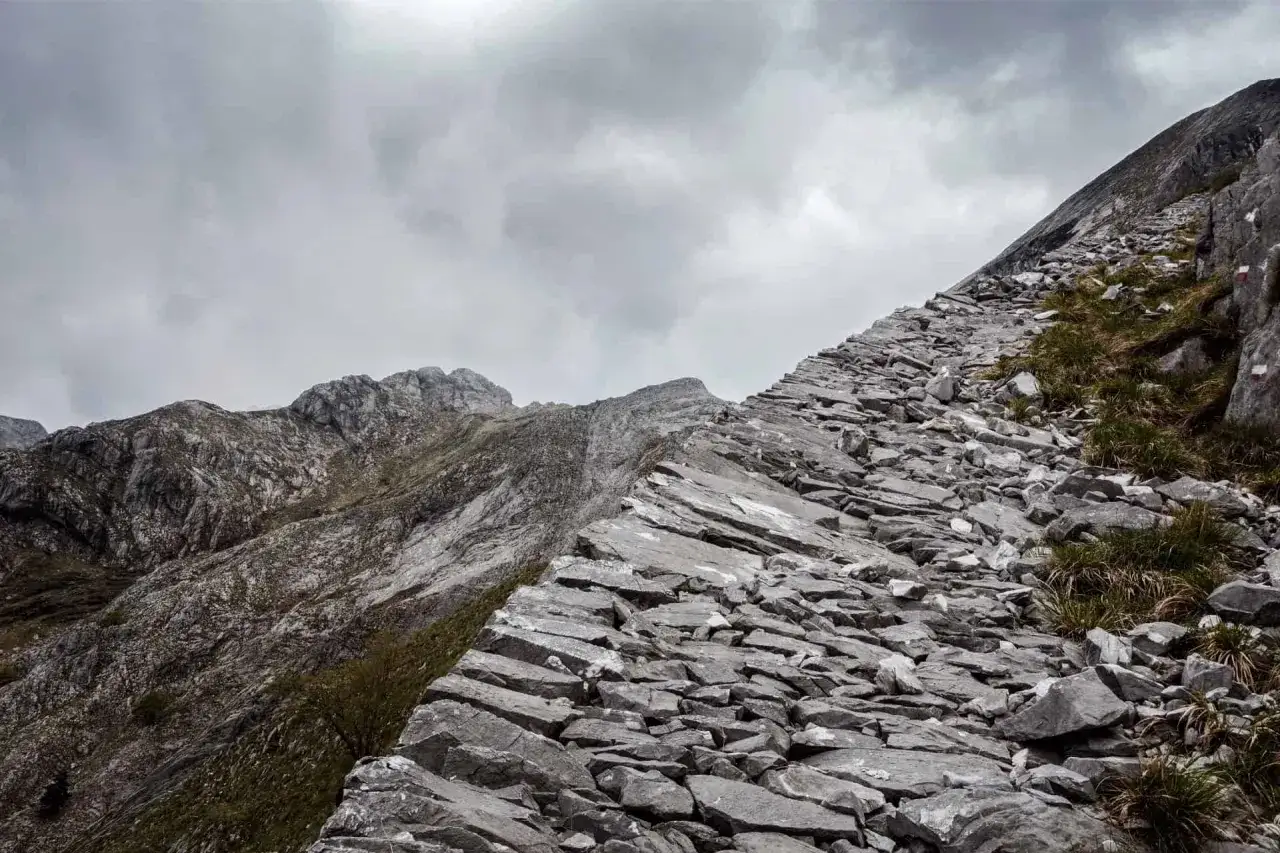 Sentiero roccioso e scosceso su la via Vandelli, con montagne grigie e cielo nuvoloso.