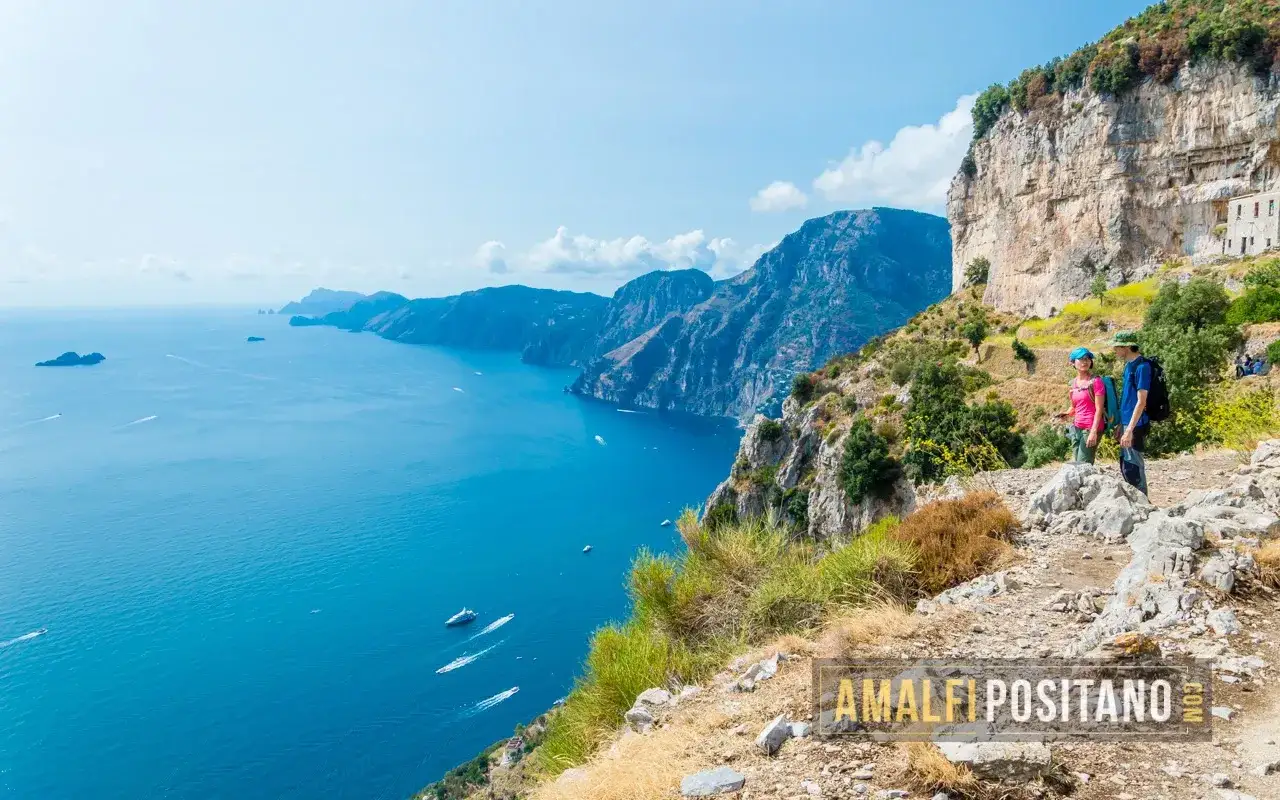 Sentiero panoramico da Amalfi a Ravello, con vista sul mare blu e montagne scoscese. Due escursionisti ammirano il paesaggio.