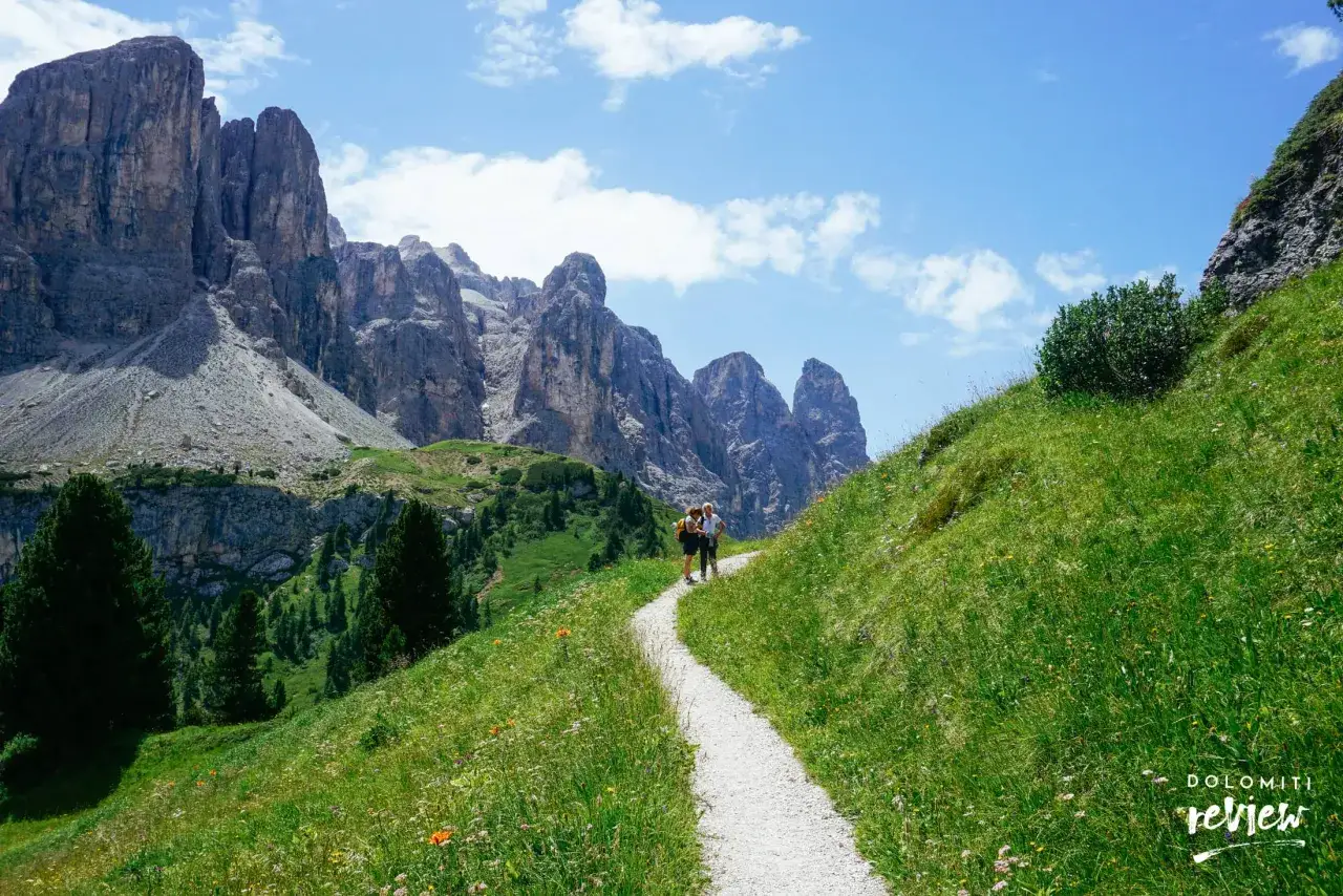 Due escursionisti su un sentiero tra prati fioriti e imponenti vette rocciose. Un'avventura indimenticabile tra le montagne.