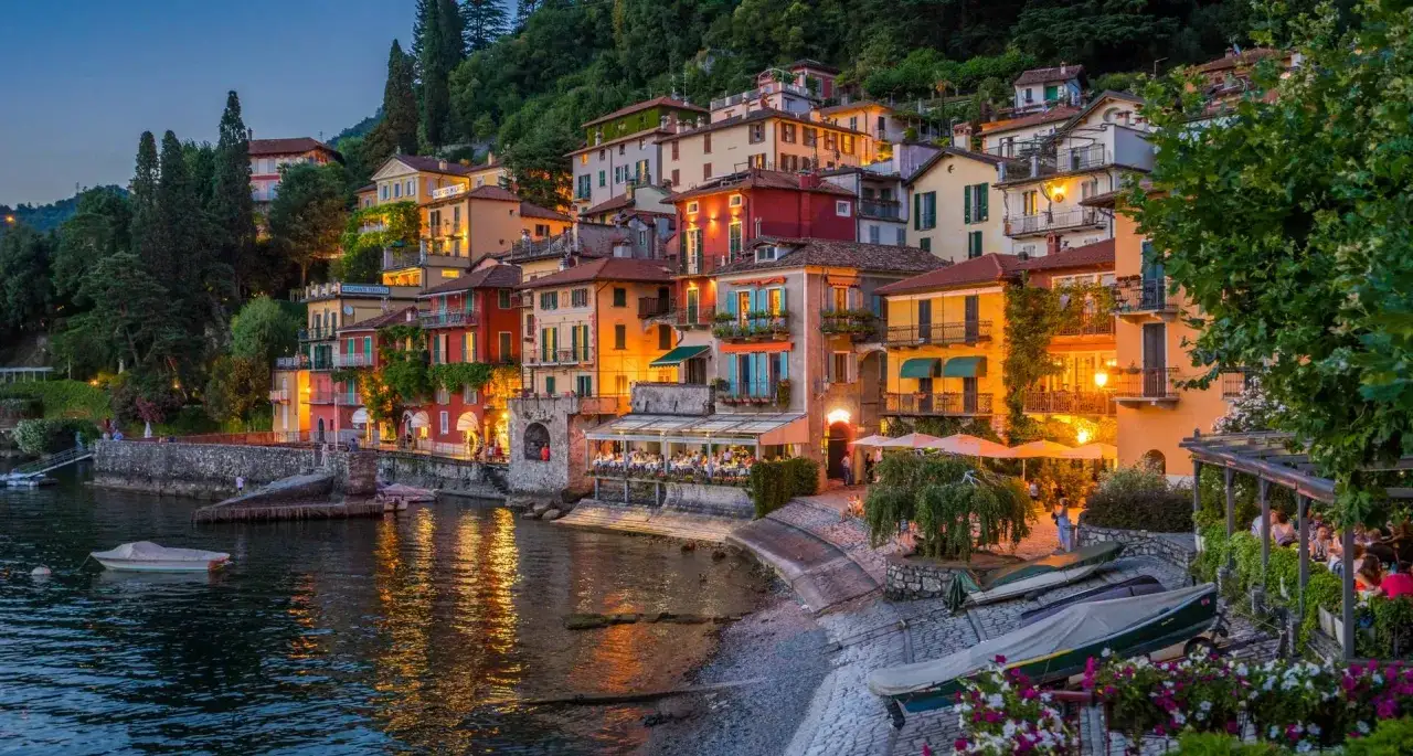Varenna centro storico illuminato al tramonto, con case colorate affacciate sul lago e ristoranti all'aperto.
